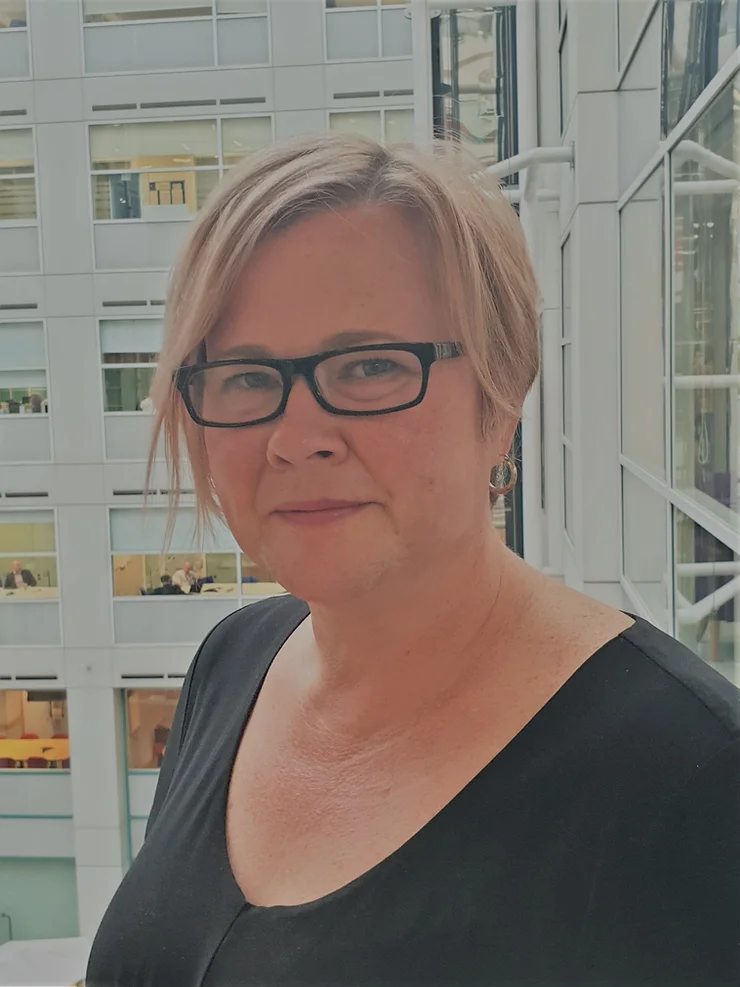 Woman smiling, wearing a black t-shirt and black glasses.